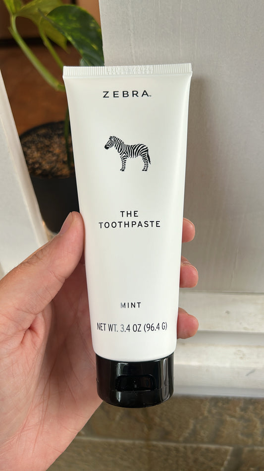 A tube of Zebra brand toothpaste with the text 'The Mint Toothpaste' and 'Zebra' branding, held in a hand against a light background.